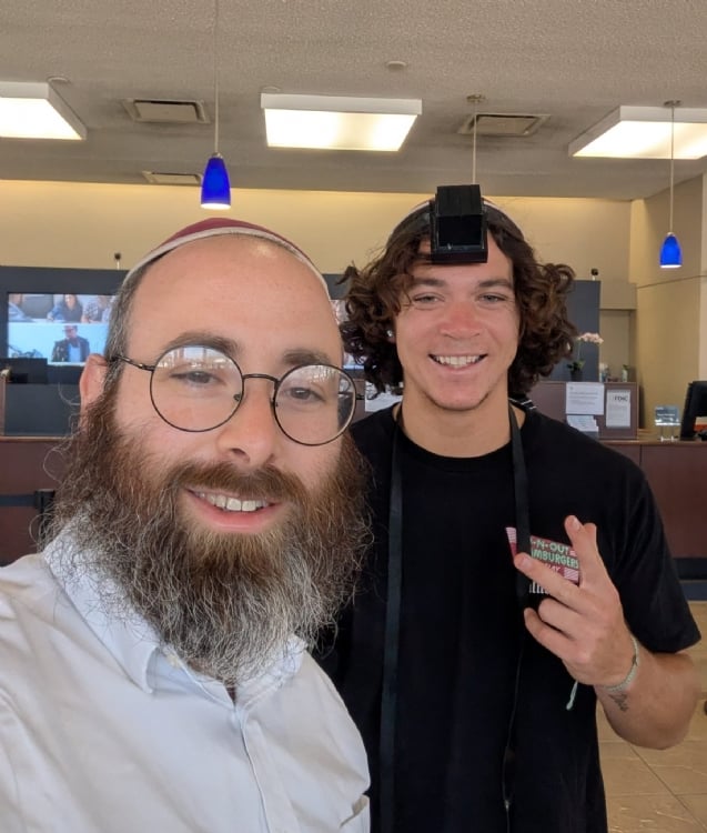 A community member smiling in tefillin beside Rabbi Stiefel